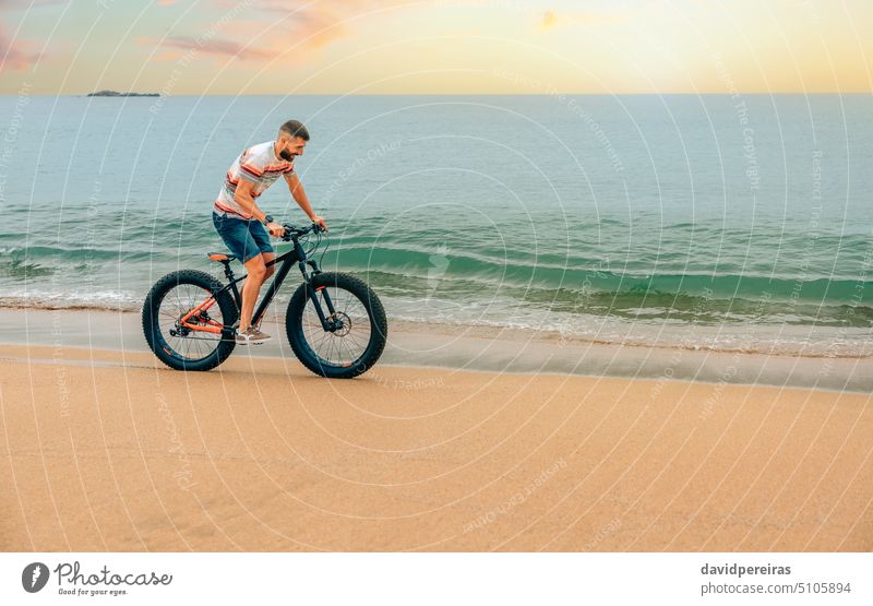 Young man riding a fat bike on the beach young seashore copy space smiling enjoy fun sand person scenery playing sport bicycle lifestyle active bicyclist