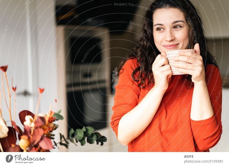 Young happy woman enjoying a hot drink in the kitchen coffee cup tea beverage female standing looking away dreamy home lifestyle holding cheerful girl portrait