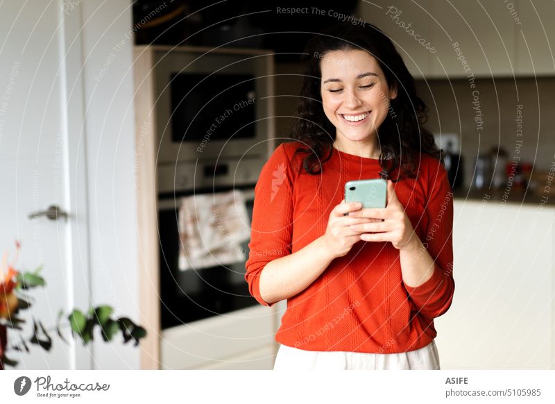 Young happy woman using her phone in the kitchen home smiling smartphone mobile laughing smile young talking attractive communication telephone internet
