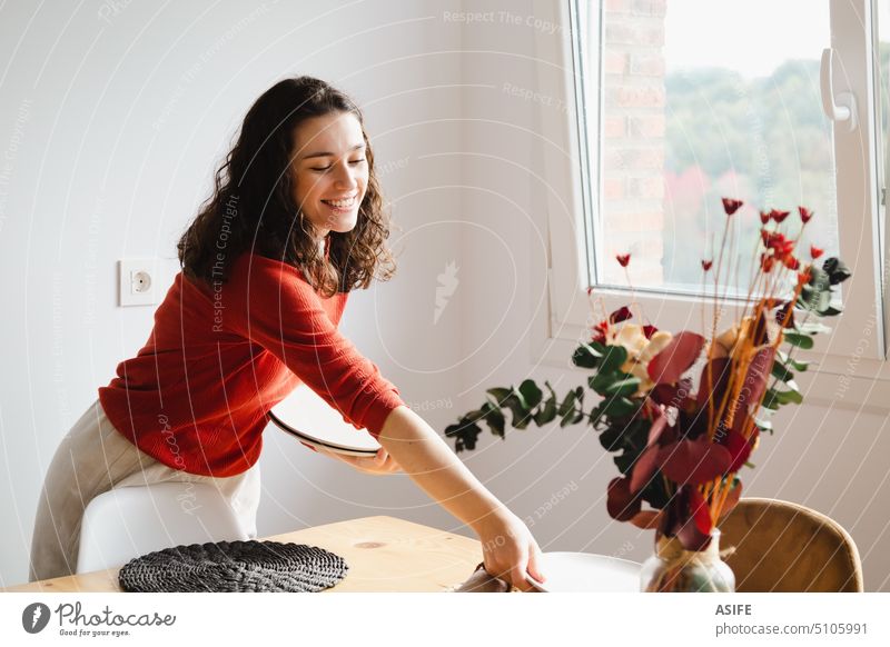 Young happy woman setting the table at home place decorating flowers tableware dining dish wooden dishware dried flowers eucalyptus vase bouquet young beautiful
