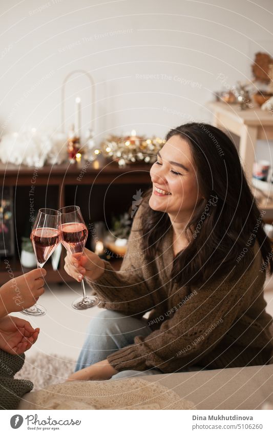 Young adult caucasian woman cheering with sparkling wine with her friend or partner, smiling and laughing. Women celebrating holiday and drinking. St Valentines's Day or Christmas holiday season celebration at home apartment.