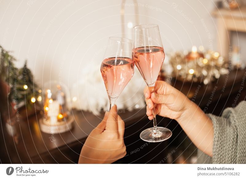 Holding two glasses of rose sparkling wine to cheers for Christmas or New year. Celebrating at party. Happy Birthday or anniversary. Festive drinks background. Feasts and celebrations. Cheering with glasses. Horizontal New Year party background.