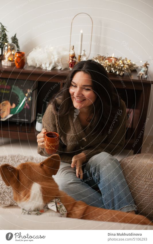 Adult brunette caucasian woman playing with corgi dog and drinking coffee at home apartment decorated for Christmas holiday season. beautiful happy attractive