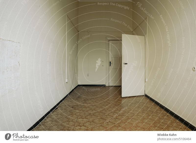 narrow and sparse room. With old linoleum floor. White dingy wall with cable strips and sockets. One open door and one closed door in the background. empty room