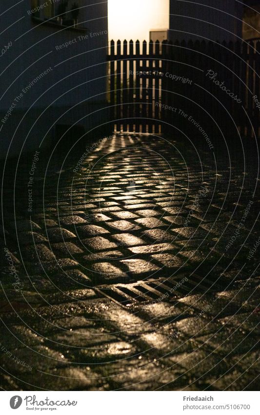 In the rain shiny cobblestones off Paving stone Glittering Evening Rain Light and shadow Shadow Fence Contrast Exterior shot Calm Moody Street Ambience Town