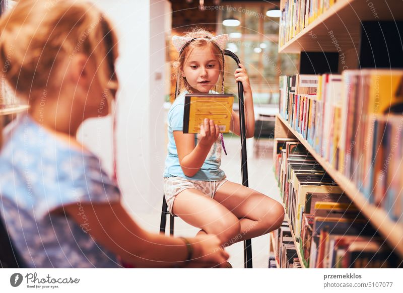 Schoolgirls looking for audio books in school library. Students choosing books. Elementary education. Doing homework. Back to school back schoolgirl child