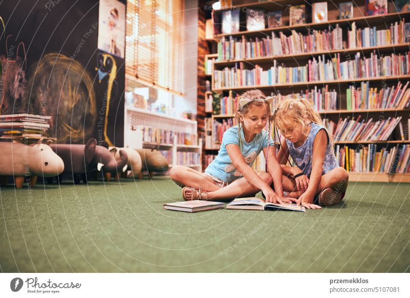 Two elementary school students reading books in the school library. School girls learn from books. They are doing homework. Children having fun. Back to school