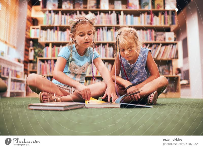 Two schoolgirls reading books in school library. Primary school students learning from books. Pupils doing homework. Children having fun in school club. Back to school