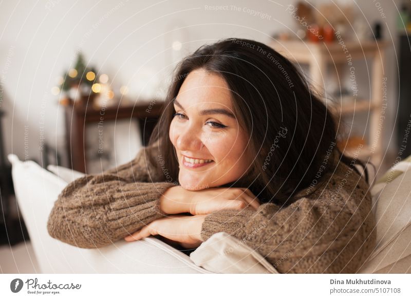 Beautiful caucasian woman smiling at her cozy home apartment leaning over the couch. Closeup casual lifestyle female portrait. Millennial living. Expat life. Creating comfortable space around you.