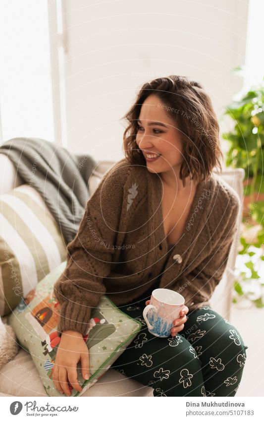 Beautiful young caucasian woman with brown hair at cozy home apartment. Casual portrait of a woman with a drink on a couch comfortable christmas beautiful happy