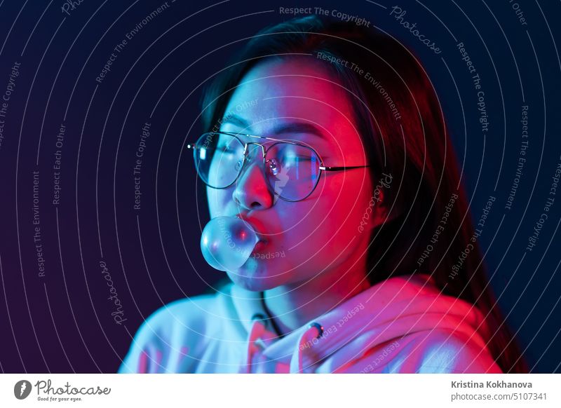 Young pretty asian girl with cute face inflates the chewing bubble in glowing pink neon light of the city at night. Hipster teenager concept. glamour fashion