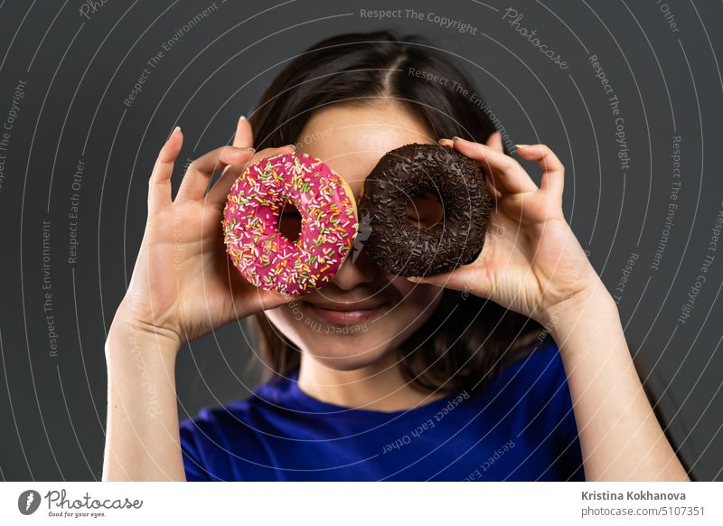 Portrait of cheerful beautiful asian woman dancing with sweets colorful donuts isolated on grey studio background. Concept of joy, food, lifestyle. person girl
