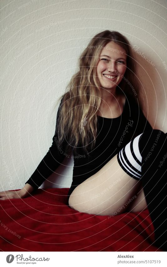 Portrait of a young slender blonde woman wearing dress and long overknees sitting on a red blanket and smiling portrait Woman Young woman Legs Sock Dress Blonde