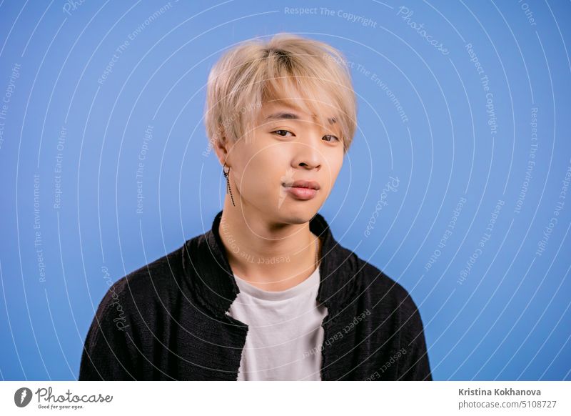 Portrait of stylish korean man looking to camera. Asian guy with dyed blonde hairstyle in studio on bright blue background. adult horizontal person