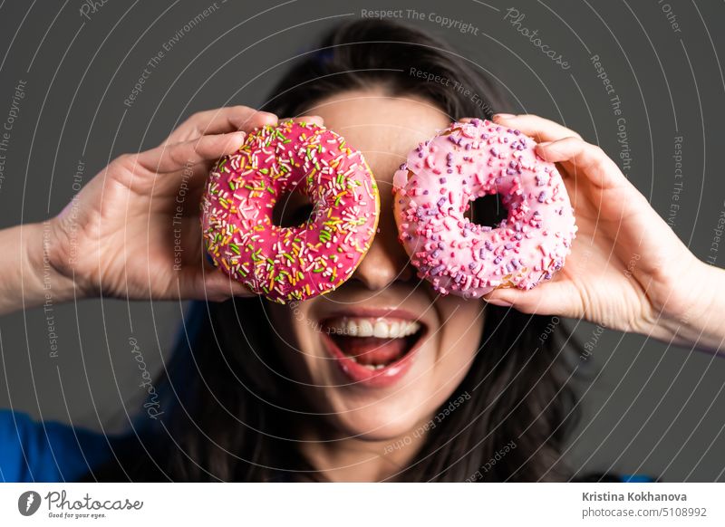 Portrait of cheerful beautiful woman dancing with sweets colorful donuts isolated on grey studio background. Concept of joy, food, lifestyle. person girl