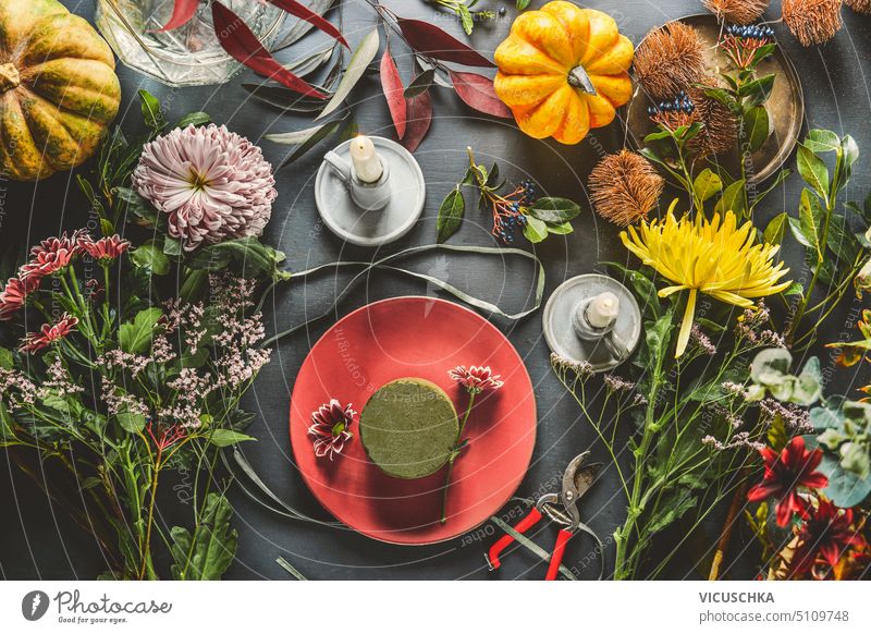 Various flowers with pumpkins, candles and floral foam on dark table, top view. Autumn flowers arrangement making. various autumn indoors workplace arranging