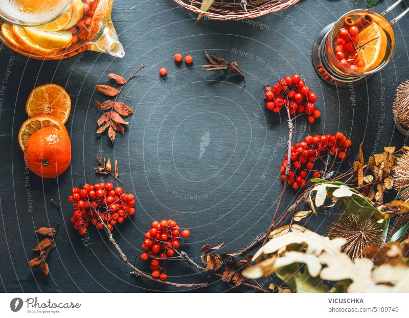 Herbal tea background frame with rowan berries, orange slices , glass teapot and cup on dark rustic background. Top view herbal top view rowanberry cozy