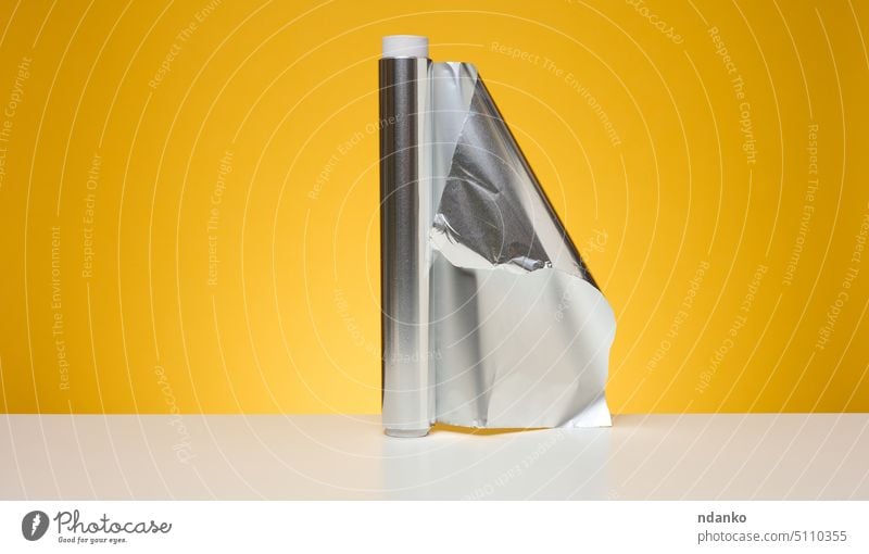 Roll of twisted food foil for packaging food on yellow background folded roll scroll sheet shine gloss aluminium aluminum blank glossy gray grey industrial