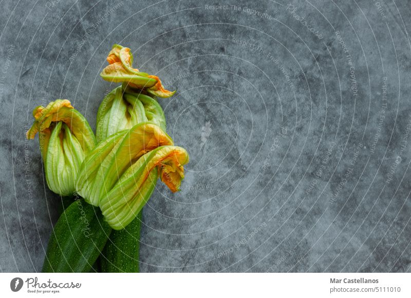 Three zucchini flowers piled on a stone background. vegetable three horizontal photo top view stone effect courgette green healthy harvest yellow vegetarian