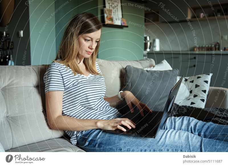 Woman at home using laptop. Remote work at home office freelancer woman remote browsing online concentrated working living room couch lifestyle bright computer