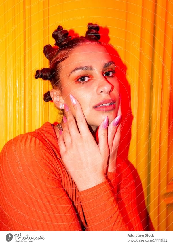 Trendy woman with bantu knots in studio style trendy touch chin eyes closed neon light dreamy accessory sweater charming calm young illuminate appearance female