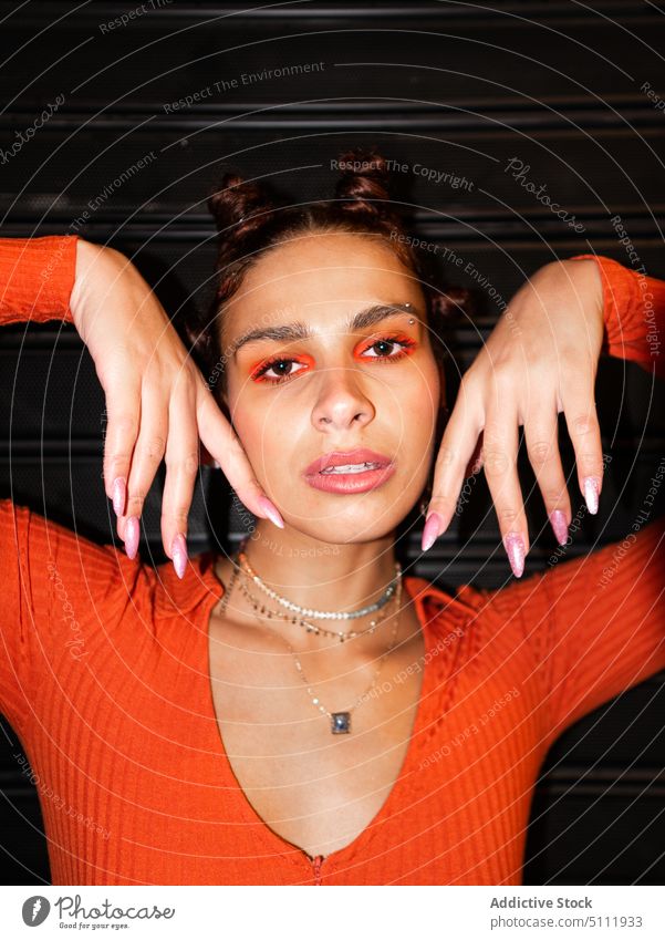 Stylish woman touching face and looking at camera serious trendy mouth opened makeup eyeshadow orange style accessory portrait bantu knots fashion appearance