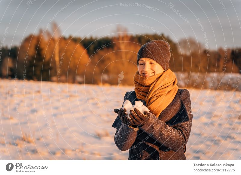 Smiling woman in a scarf and hat holds a handful of snow in winter warm clothes female people person European White adult mid adult one Single person orange