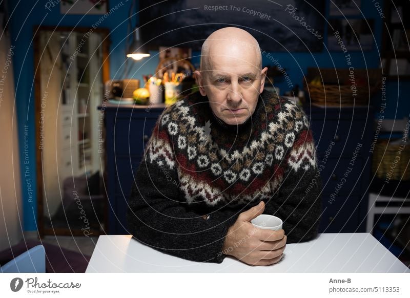 my friend sits with a very serious face with the coffee cup at the kitchen table and has, because we hardly heat, a thick Icelandic sweater on Man sedentary