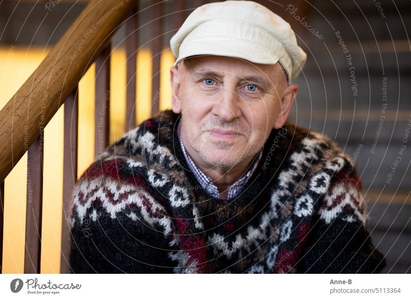 Portrait of friendly satisfied looking man sitting in a stairwell with cap and knitted sweater Masculine Man Adults 1 Human being 45 - 60 years Shirt Cap