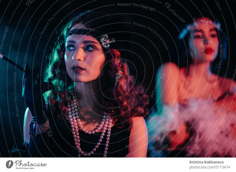 Portrait of young flapper women dressed in style of Great Gatsby posing on dark velours background. Roaring twenties, retro, party, fashion concept 1920s