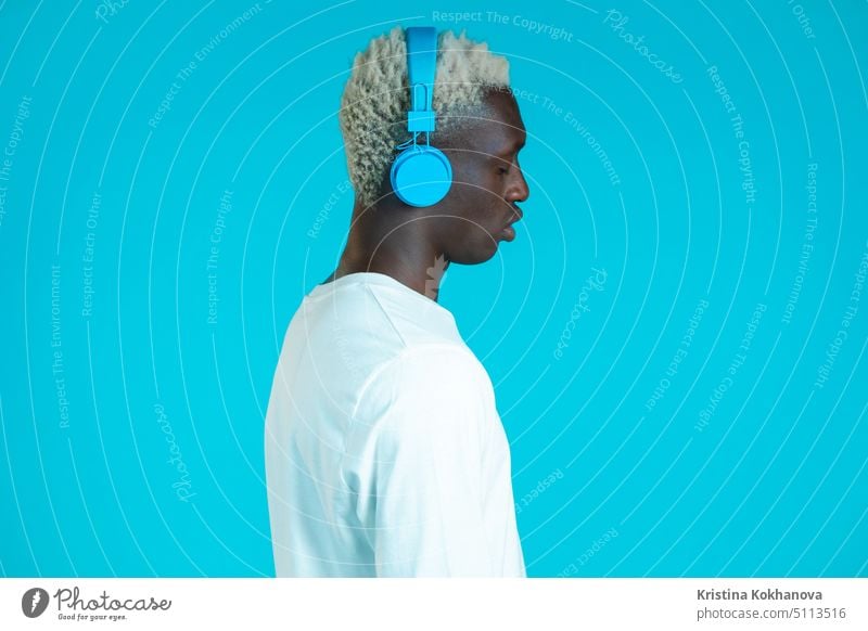 Handsome black man with trendy hairdo and headphones in studio against blue background. Music, dance, radio concept. person listening music beautiful adult