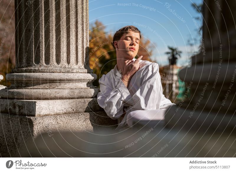 Calm homosexual man leaning on pillar in autumn park androgynous eyes closed lgbt dreamy column non binary portrait gender fluid pensive male young makeup