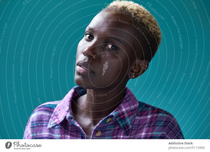 Black woman with blond short hair against turquoise background touch hair style appearance checkered shirt casual portrait colorful bright female young black