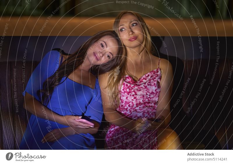 Mother and daughter on bench at night women mother lean together weekend dark nightlife female middle age mature young smartphone style dress evening event