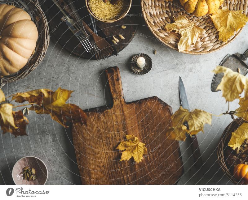 Autumn cooking background with wooden cutting board, yellow autumn leaves, knife and pumpkin on concrete kitchen table. Seasonal cooking at home. Top view.