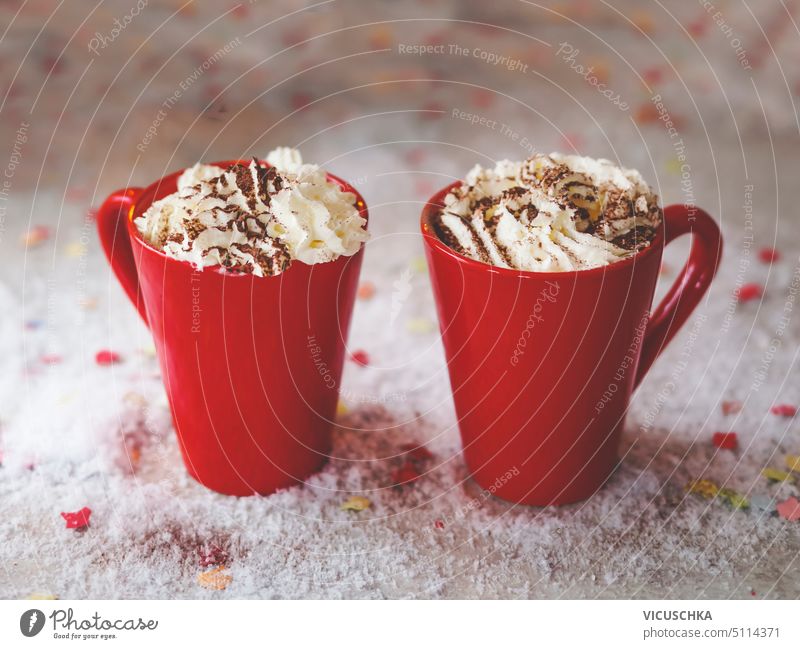 Two red mugs with hot chocolate and whipped cream on table with snow. Cozy warm drinks at home with sweet cream. Front view. two cozy front view beverage bokeh