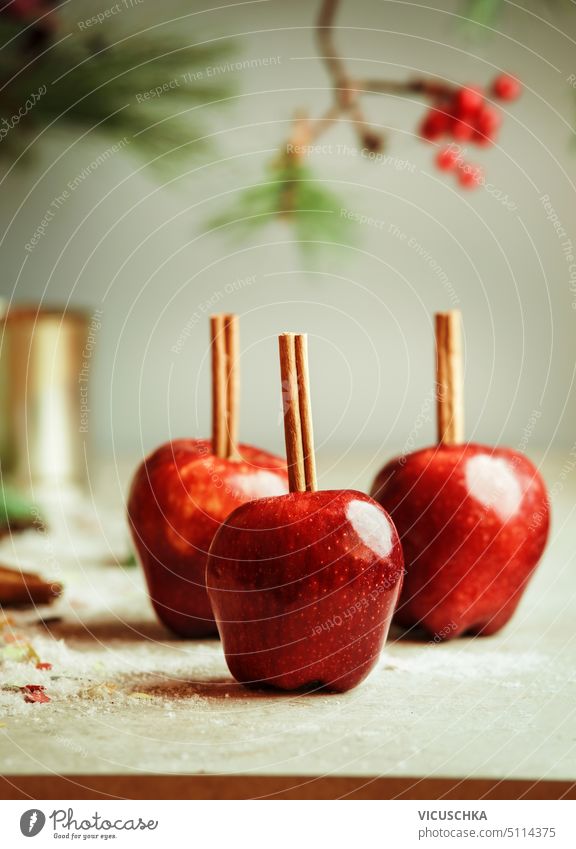 Red apples with cinnamon sticks on kitchen table with sugar at wall background with fir green. Sugar glazed apples. Delicious Christmas sweets. Front view. red