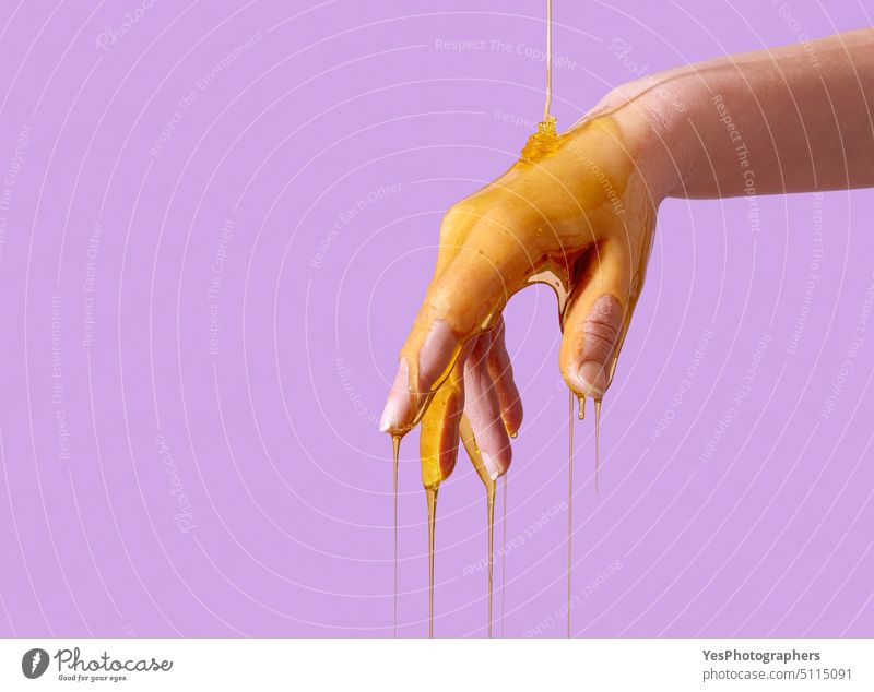 Skin care concept, pouring honey over hand, isolated on a purple background aging antioxidant arm beauty bee body bright close-up color copy space cosmetics