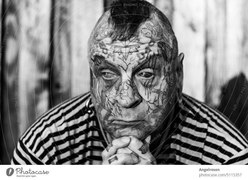 A man completely tattooed in the face, with a thoughtful expression. Even his eyeballs are not white, because they are colored by means of eyeball tattoo. Image: in B&W and high contrast.