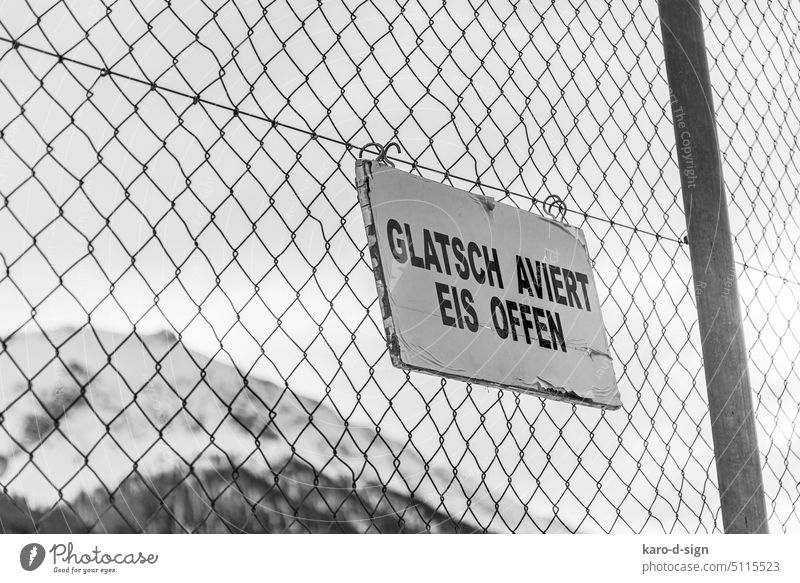 Fence ice rink with sign Black & white photo Winter mood Ice-skating Rhaeto-Romanic Grisons Switzerland Winter sports mountain worlds structures