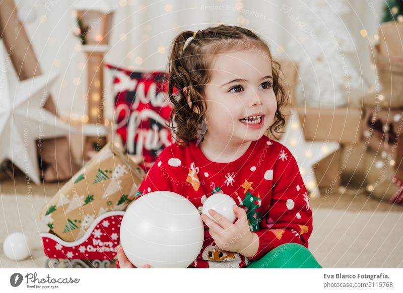 smiling little girl at home holding baubles during christmas time child presents happy gift cheerful cute 2 kid children family december decoration indoors