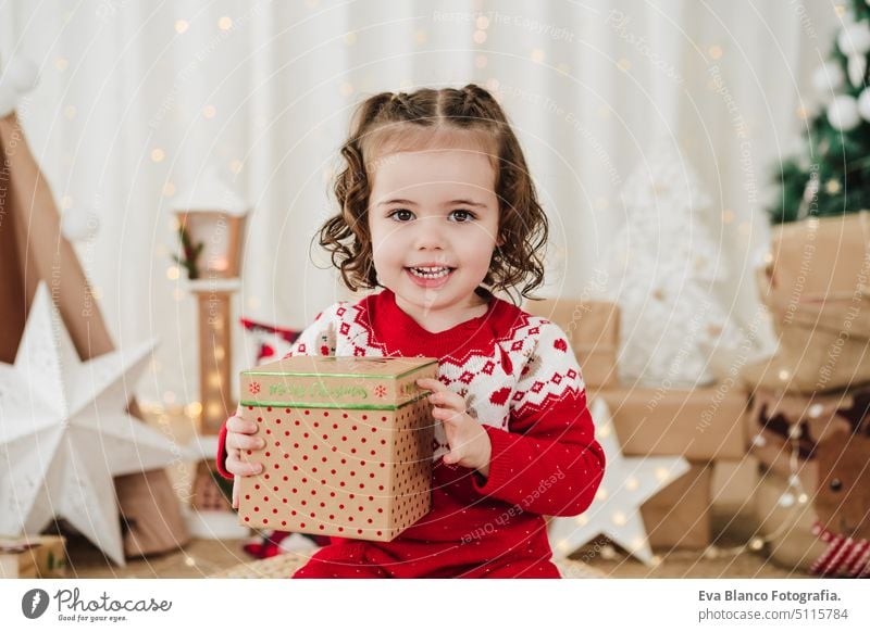smiling cute little girl at home during christmas time holding gift box child presents happy cheerful 2 kid children family december decoration indoors smile