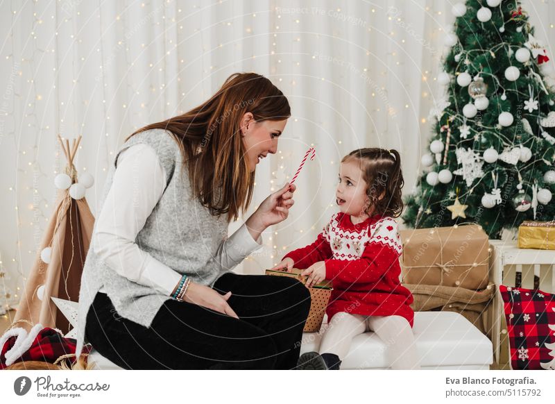 cheerful mother and daughter at home enjoying christmas time at home. giving candy to child family living room love together motherhood single mother caucasian