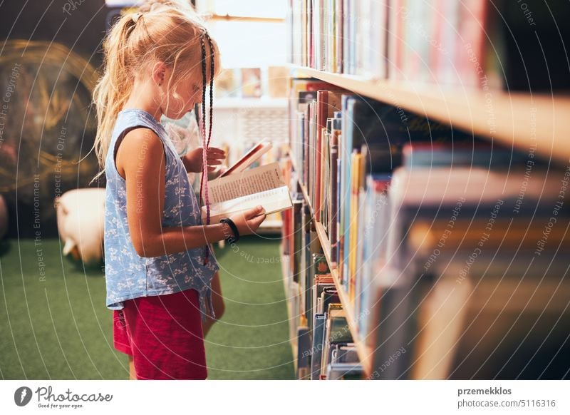 Schoolgirl looking for book for reading in school library. Student choosing literature for reading. Books on shelves in bookstore. Learning from books. Back to school. Elementary education