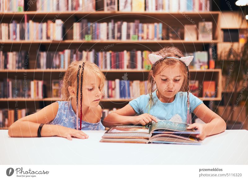 Two elementary schoolgirls doing homework in school library. Students learning from books. Pupils having fun in library. Back to school back student studying