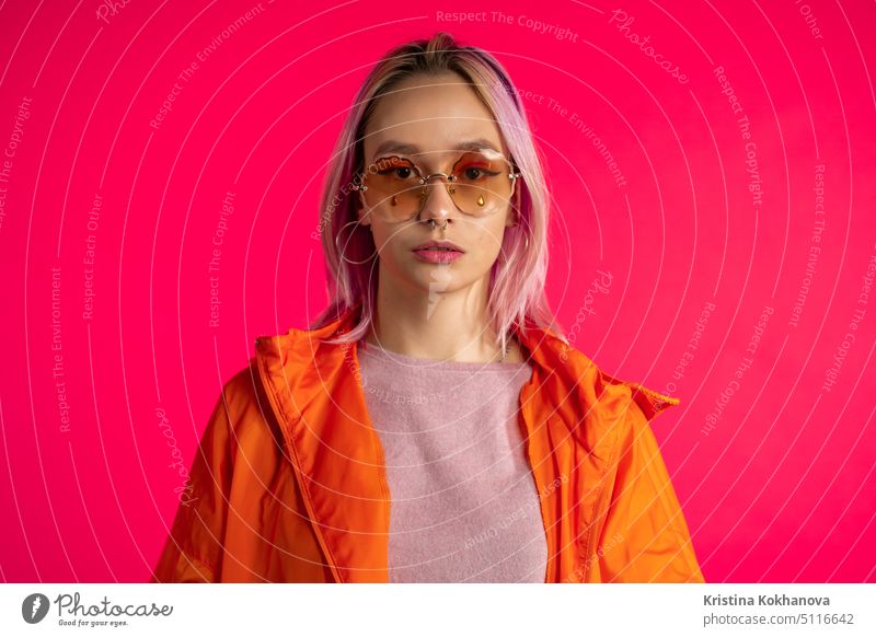 Portrait of pretty unusual woman with dyed hair on viva magenta studio background. Trendy neon colorful woman with piercing, eyewear. Vibrant shot. attractive