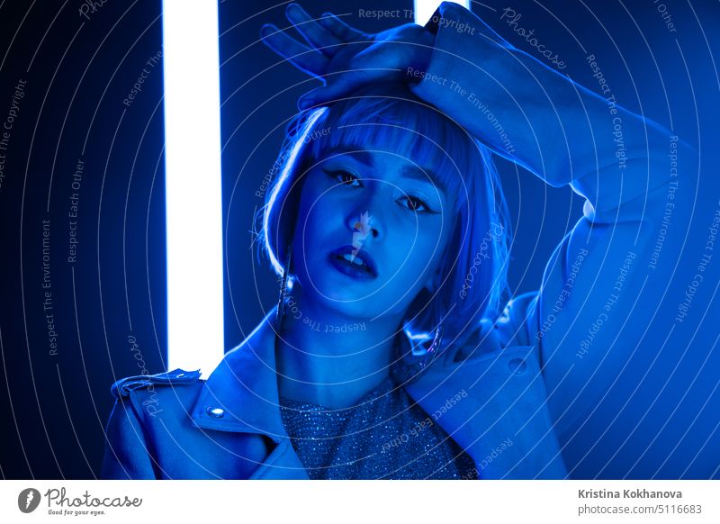 Charismatic woman with bob haircut posing near led-blue neon lamps. Hipster trendy girl. Modern model pop outfit, influencer lifestyle. listening dance party