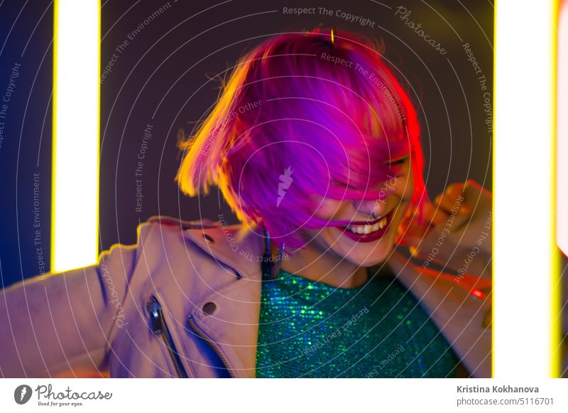 Amazing smiling woman with dyed pink hairstyle dancing on led-colorful neon lamps background. Charming lady, night life concept. Modern pop outfit, influencer lifestyle.