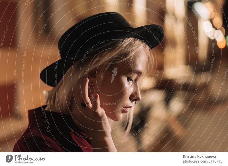 Portrait of young woman with blond hairstyle and hat on night glowing european city background. Nose piercing. person nightlife lifestyle female girl beautiful