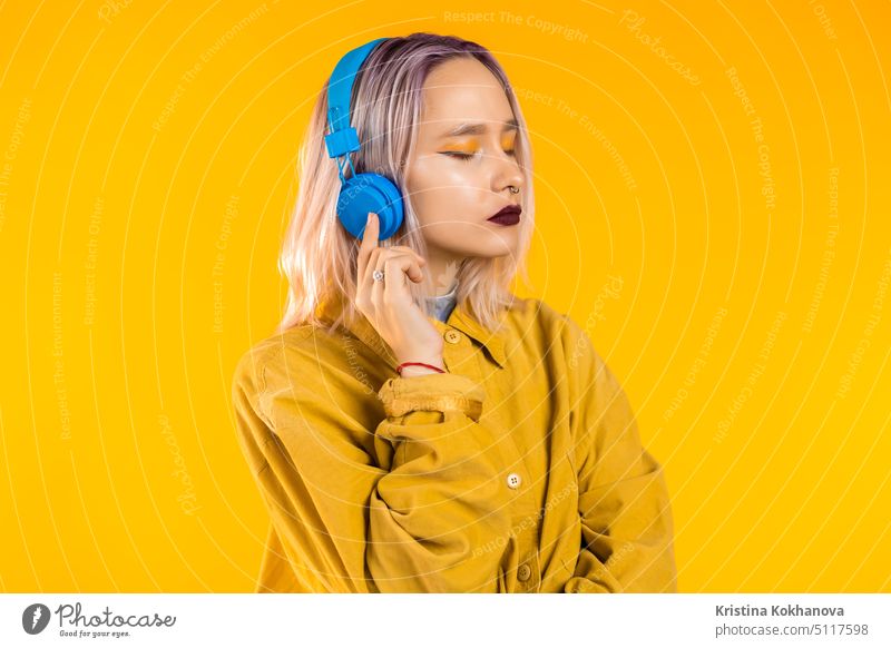 Beautiful woman with pink hair dancing with headphones on yellow studio girl teen emotions unusual trendy stylish female make-up beautiful cute person adult